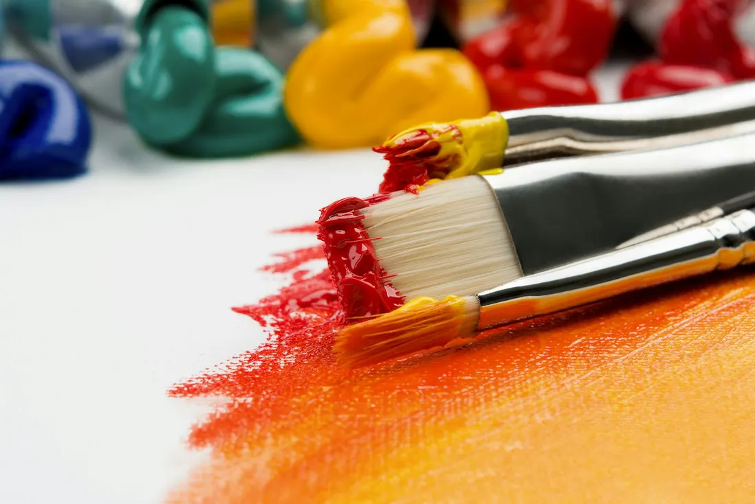 Paint brushes loaded with bright colours on textured paper